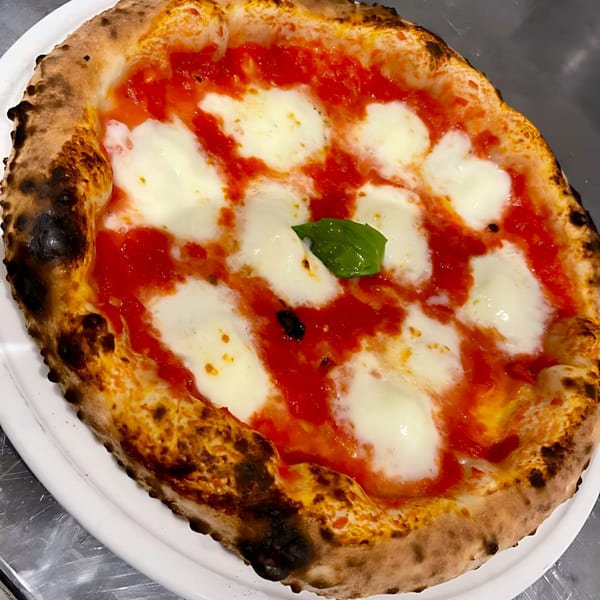 A Neapolitan pizza with bubbly crust, melted mozzarella, vibrant tomato sauce, and a fresh basil leaf.