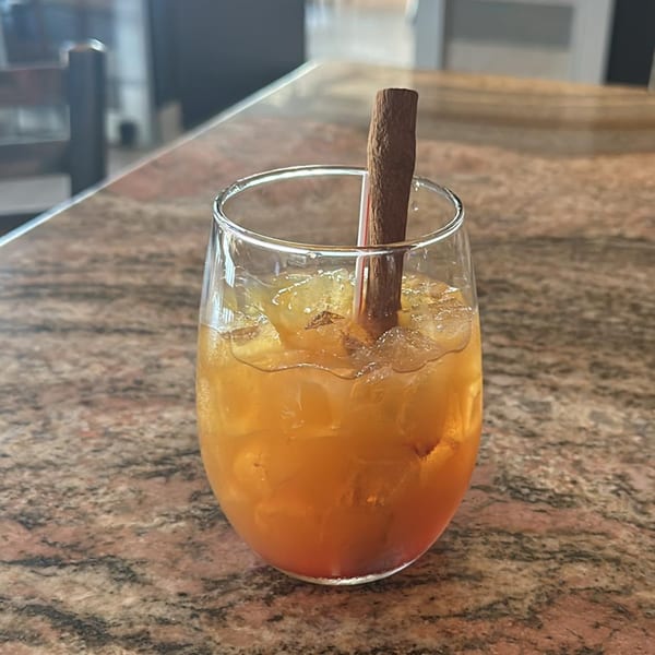 A glass of iced orange drink with a cinnamon stick on a marble counter.