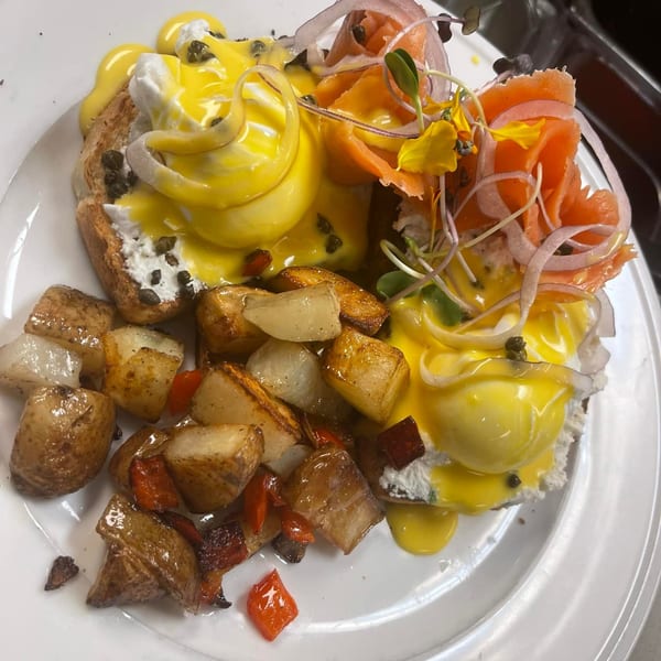 Eggs Benedict with smoked salmon, hollandaise sauce, capers, red onions, and roasted potatoes on a white plate.