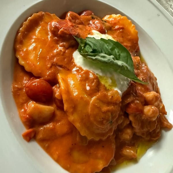 Ravioli in a rich orange sauce with cherry tomatoes, a dollop of white cheese, and basil.
