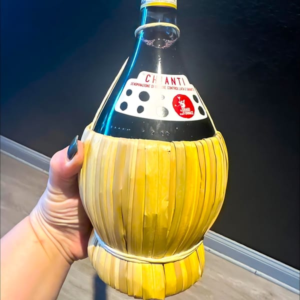 A hand holds a traditional straw-covered Chianti wine bottle from Manny's Cucina Napoletana.